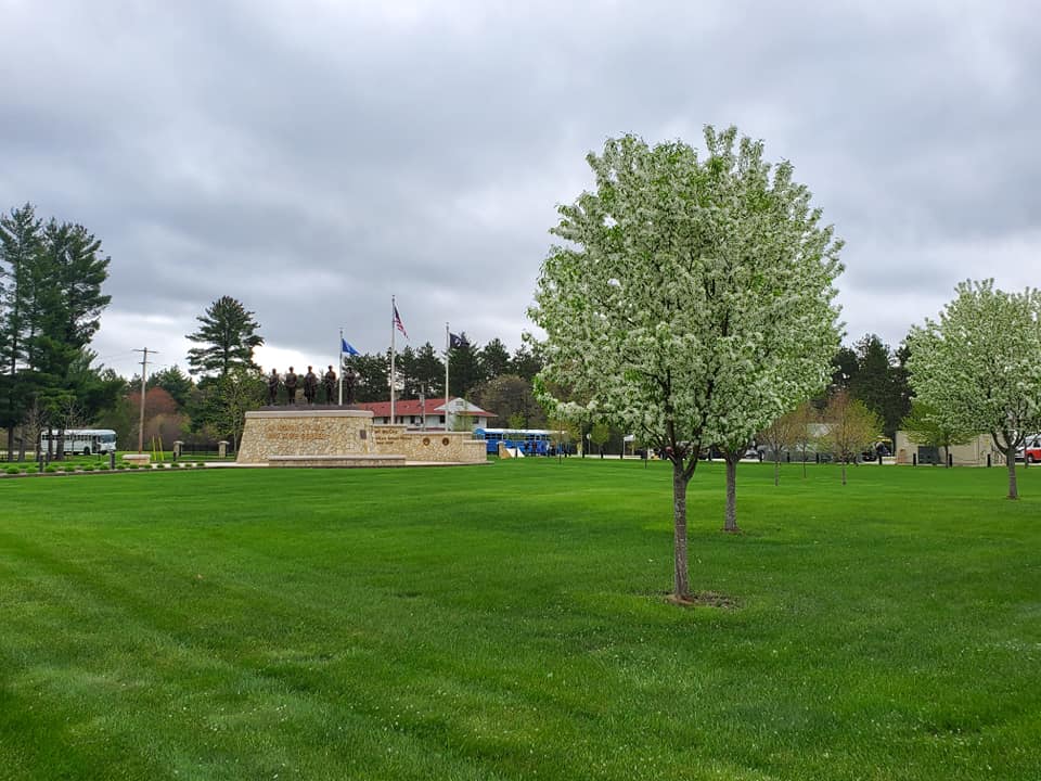 A field full of green grass with Fort McCoy's Historical Center stone sign in the background.